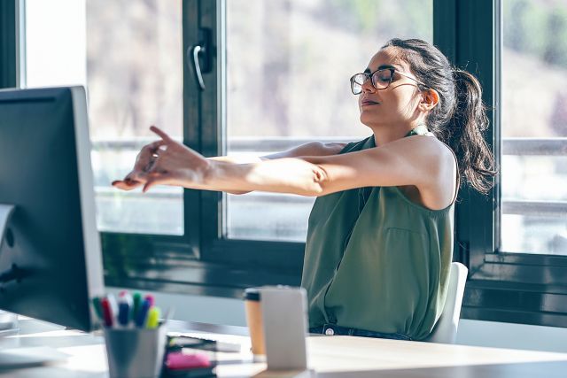 An office professional demonstrating ergonomic posture at a modern standing desk setup, emphasizing workplace wellness